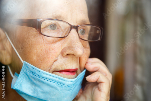 Portrait of an elderly woman in a window after quarantine with her mask removed. An old woman in a window with her mask down, after the pandemic.