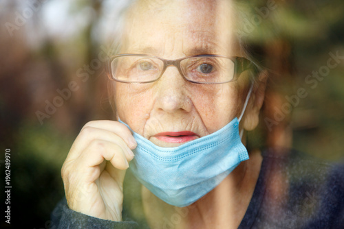 Portrait of an elderly woman in a window after quarantine with her mask removed. An old woman in a window with her mask down, after the pandemic.