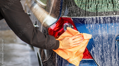 Hand cleaning car tail light with microfiber cloth and soap foam, car washing and detailing process, vehicle care and maintenance concept outdoors