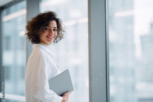 Free Download Confident young woman smiling while holding a tablet, suggesting modern work ethic and digital communication. - GFXLoad