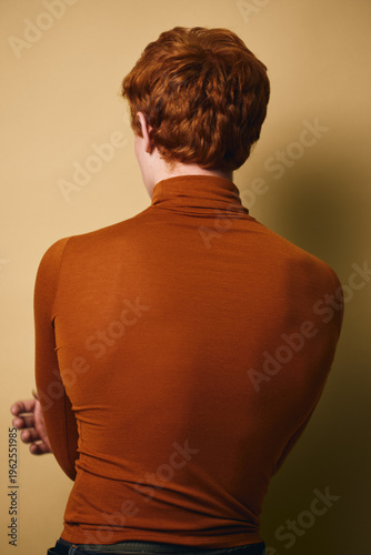 Foto Person with red hair facing away in brown turtleneck sweater against beige background