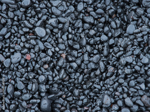 High-angle full-frame background of smooth wet black volcanic pebbles - Natural textured dark stones and gravel, perfect for geology, nature, or abstract design backgrounds.