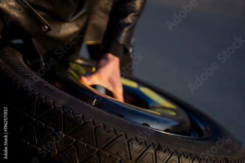 Hand positioning spare wheel on car hub, closeup of tire alignment during installation process in vehicle repair.