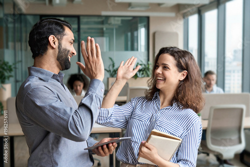 Two happy friendly diverse professionals, teacher and student giving high five standing in office celebrating success, good cooperation result, partnership teamwork and team motivation in office work.