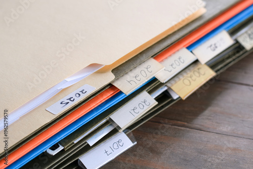 Closeup stack of file folders with past year numbers written on tabs. Organized document storage highlighting archiving, record keeping, and chronological filing system