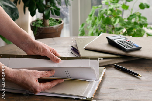 Woman hands searching through file folder on table in home setting. Documents and paperwork visible, highlighting organization, record keeping, and everyday administrative tasks.
