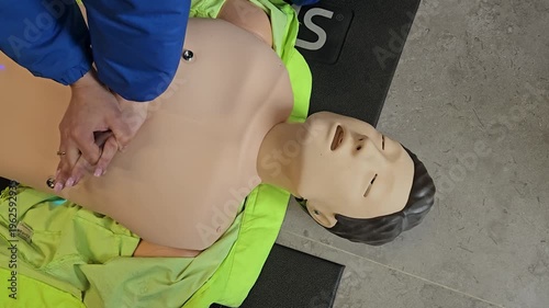 Man is performing CPR on a mannequin. The mannequin is wearing a green jacket