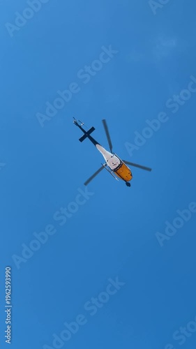 Yellow and white helicopter flying in clear blue sky. Bottom view of a civil helicopter in flight against a solid blue sky background in the USA.