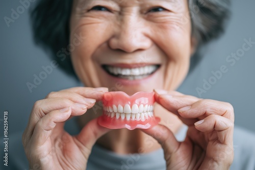 Happy Asian Senior Woman Showing a Close-up of a Denture Model