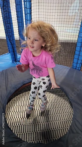 Young girl is standing on a trampoline with a giraffe shirt on. She is smiling and she is enjoying herself