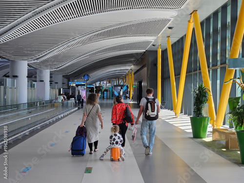 Family of four is walking through an airport terminal with luggage. Scene is that of a family traveling together, possibly on vacation
