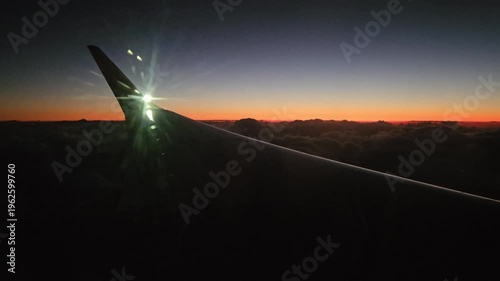 Red tail of an airplane wing is seen in the sky. The sky is dark and the sun is setting