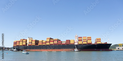 Large container ship with stacked cargo assisted by tugboats at Port of Santos, Brazil, representing global trade and maritime logistics.