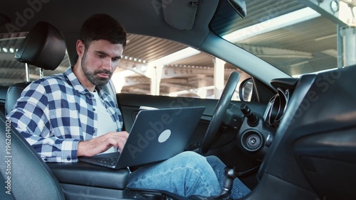 Smiling man typing on laptop and drinking coffee in the car. Slow motion