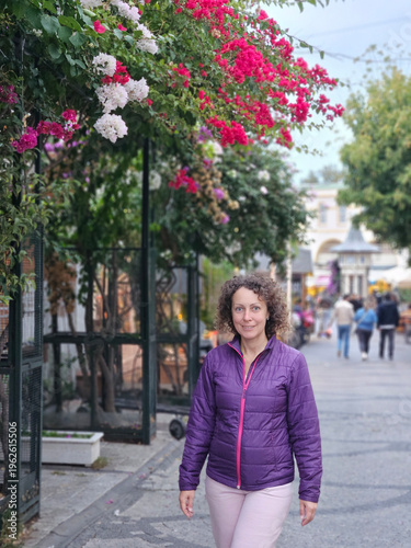 Wallpaper Mural Woman wearing a purple jacket walks down a street with a pink bush in the background. The scene is peaceful and serene, with the woman looking up at the sky Torontodigital.ca