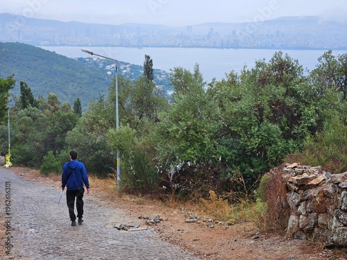 Wallpaper Mural Man is walking on a path near a body of water. The sky is cloudy and the weather is rainy Torontodigital.ca