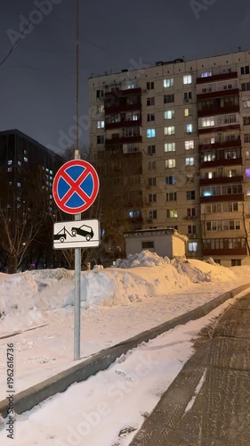 Snowy urban residential street at night with apartment buildings, road sign and winter city atmosphere