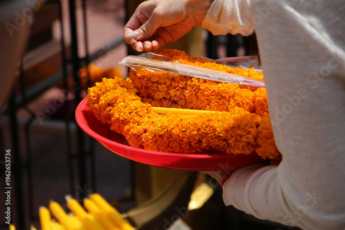 Obraz na plátně A devotee placing a marigold garland as an offering at the Erawan Shrine in Bangkok, Thailand