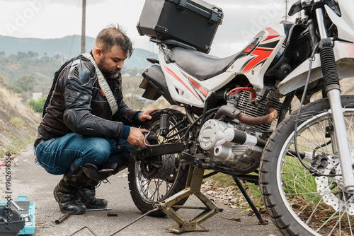 Bild auf Leinwand Biker repairing motorcycle on road after breakdown