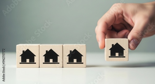 Hand holding wooden block with house icon above other blocks on table