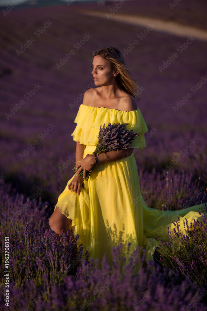 Obraz premium Woman lavender field beautiful blonde model in flowing yellow dress holding flowers at sunset