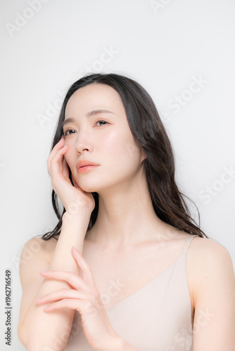 黒髪のパーマのロングヘアで白背景の若い女性のビューティーイメージ　スキンケアなどのツヤ肌、保湿や高級感のあるラグジュアリーな美容イメージアンニュイな表情