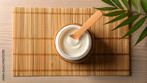 Wooden bowl with white cream and wooden spoon on bamboo mat with green leaf