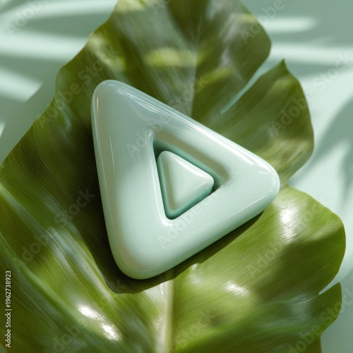 Clay Play Button in Sage Green on a Banana Leaf With Sunlight Dappling Through Trees in a Natural Setting