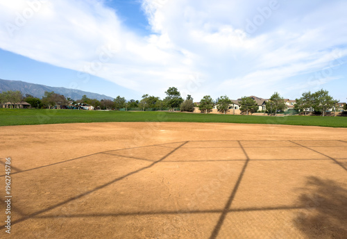 Fotografi Sunny baseball field with a sandy infield sits open and empty green grass surrou