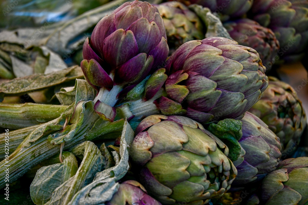 Fototapeta premium Stack of purple and green artichokes at market
