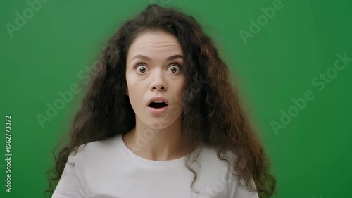 A young woman with dark, curly hair shows a surprised expression against a green screen.
