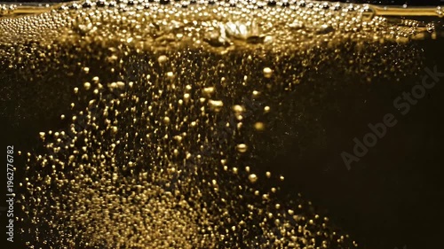 Close-up abstract view of golden bubbles rising in dark liquid