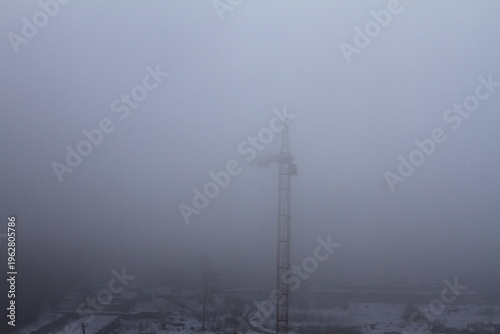 Thick fog at the construction site. Poor visibility prevents the tower crane from working.