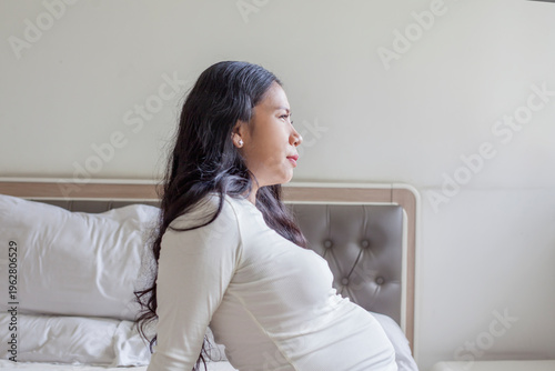 Schilderij op canvas Pregnant Asian Woman Sitting on Bed with a Pensive and Thoughtful Expression