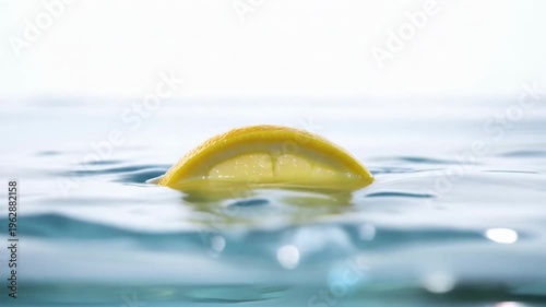 Fresh lemon slice splashing into water with droplets in slow motion