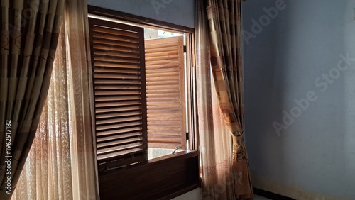 Open wooden window shutters with patterned curtains interior shot for real estate marketing home design and architectural concepts.