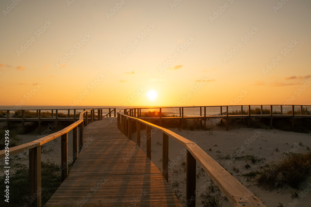 Fototapeta premium Wooden path at Costa Nova d'Aveiro, Portugal, over sand dunes with ocean view, evening. Wooden footbridge of Costa Nova beach . Aveiro, Portugal.