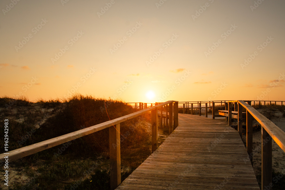 Obraz premium Wooden path at Costa Nova d'Aveiro, Portugal, over sand dunes with ocean view, evening. Wooden footbridge of Costa Nova beach . Aveiro, Portugal.