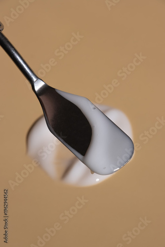 Photos Stainless steel cosmetic spatula spreading rich white cream across a smooth beige surface
