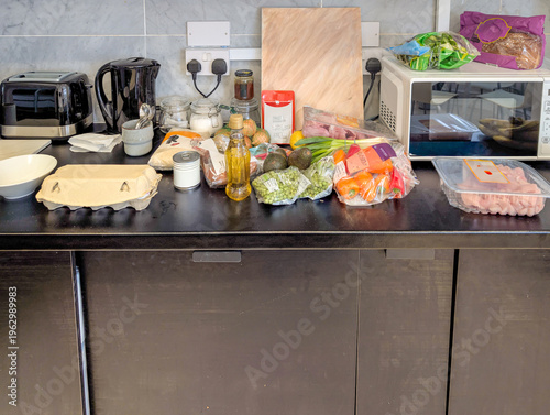 Fresh groceries and ingredients arranged on modern kitchen countertop. Assortment of raw food items including vegetables, meat, eggs, and pantry staples displayed in a contemporary home cooking space 