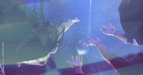 Event attendees reaching for disco ball while spotlight beam striking it, following music beat