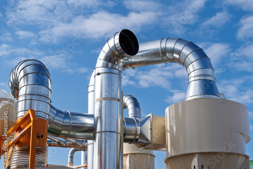 Large industrial ventilation system with galvanized steel ducts and cyclone dust collectors against a blue sky, representing factory air filtration and industrial climate control technology