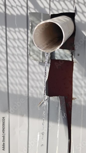 Water flows continuously from a pipe attached to a wall, showcasing a gradual increase in the stream's visibility and movement in a well-lit outdoor setting