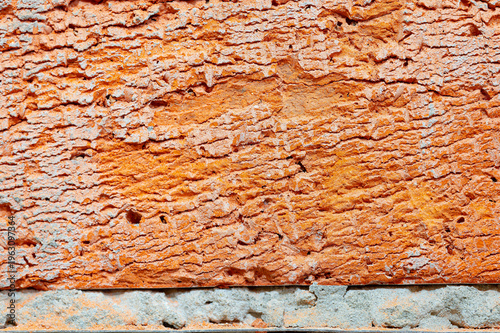 Close up macro shot of a rough textured orange clay brick surface with a line of grey cement mortar running along the bottom edge