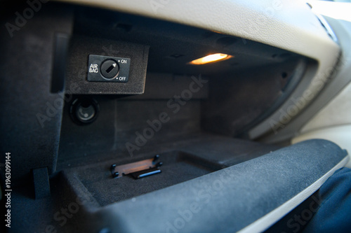 Open car glove compartment with passenger airbag on-off switch and interior light. Detailed view of automotive storage space and safety controls in a modern premium vehicle cabin.