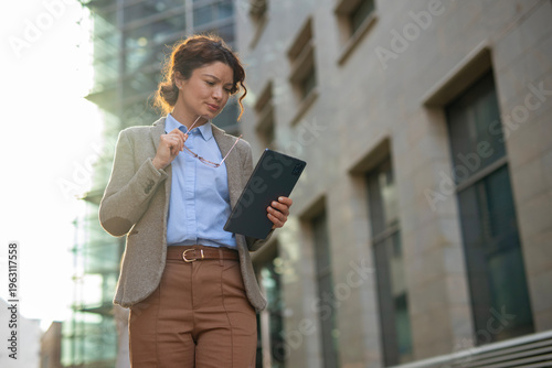 Businesswoman standing outdoors holding tablet and glasses