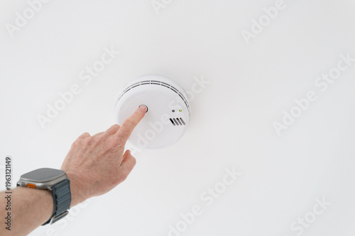 Homeowner seen pressing his finger to test a combined smoke and carbon monoxide ceiling mounted detector. The detector does not require batteries as it is mains powered.