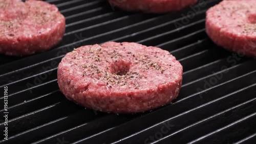 Three raw, seasoned ground beef burger patties, each with a small dimple in the center, resting on a black cast iron grill grate, ready for cooking.