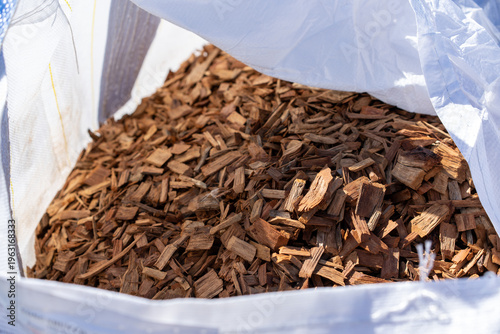 Fotografie Brown wood chips mulch in large white bulk bag close-up view outdoors in sunligh