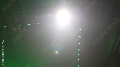 Bright green spotlights cut through the dark atmosphere of an empty stage or venue. The dynamic beams create circular patterns on the floor, evoking an energetic mood for a concert or live event.
